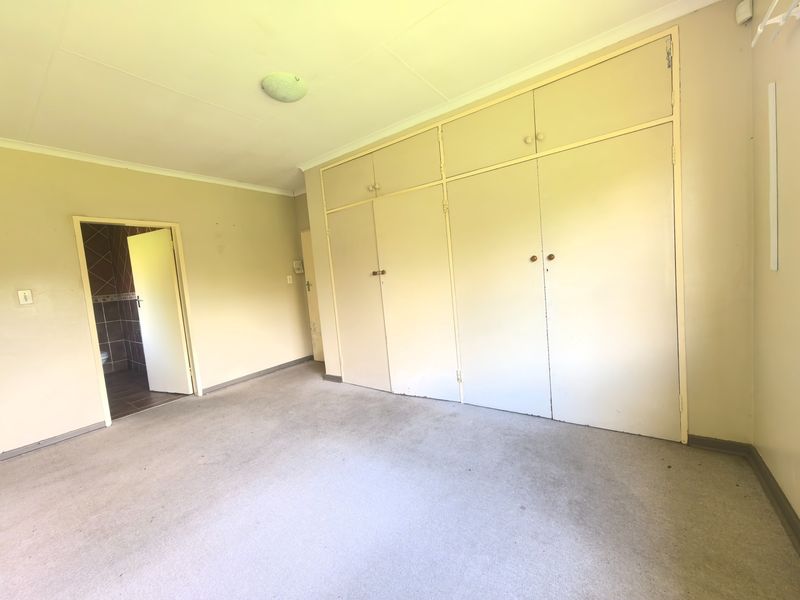 An empty bedroom featuring built-in cupboards, carpeted flooring, and direct access to an en-suite bathroom.
