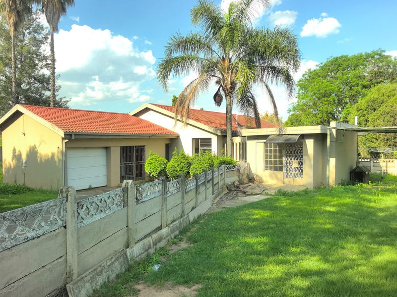 Rear view of the property featuring a tiled roof, garage access, security gates, and a precast concrete boundary wall set within a garden area.