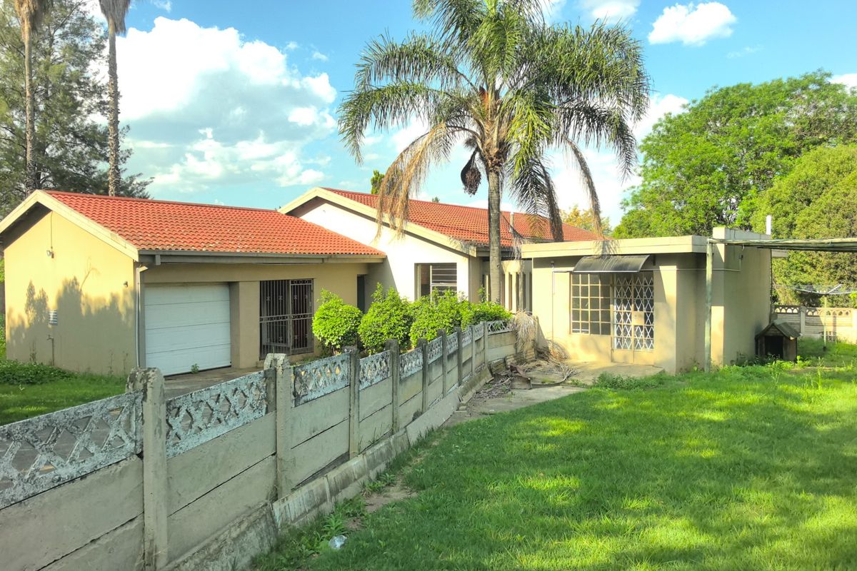 Rear view of the property featuring a tiled roof, garage access, security gates, and a precast concrete boundary wall set within a garden area.