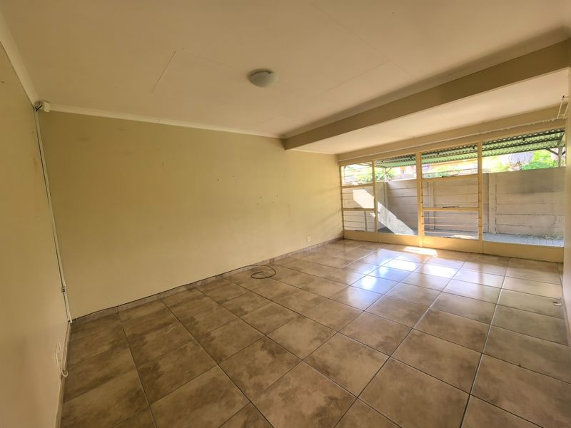 An empty, sunlit living area featuring neutral tiled flooring and large windows that provide ample natural light and access to the outdoor space.