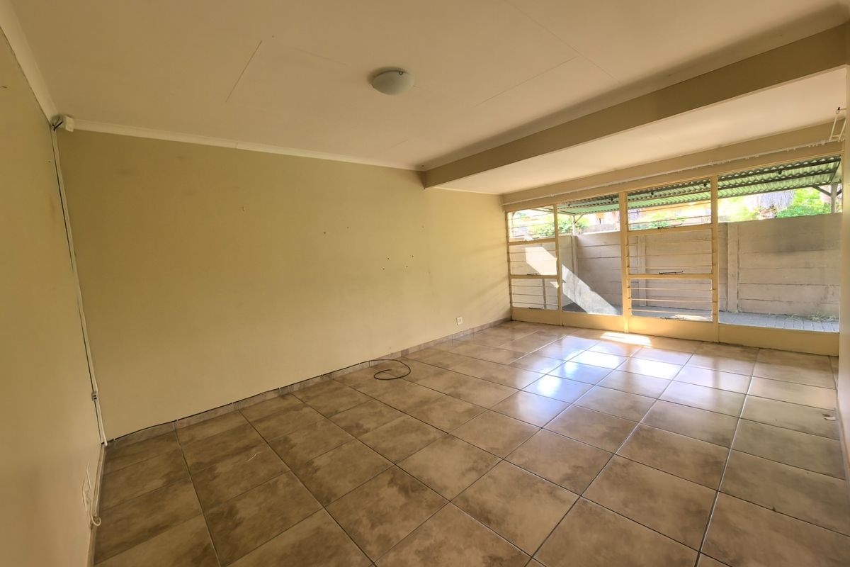 An empty, sunlit living area featuring neutral tiled flooring and large windows that provide ample natural light and access to the outdoor space.