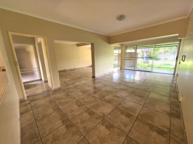 Spacious open-plan living area featuring neutral ceramic floor tiles, large sliding glass doors with security gates, and direct access to the rear garden.