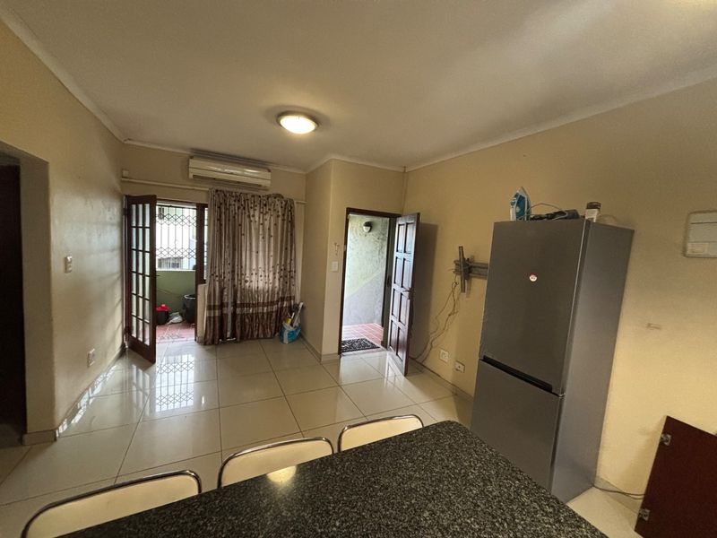 Open-plan living area featuring tiled flooring, a split-system air conditioner, and a granite breakfast counter, with direct access to an outdoor patio area.