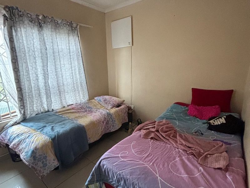 A functional bedroom featuring tiled flooring, a ceiling fan, and a wall-mounted heater, providing a practical space for residents.