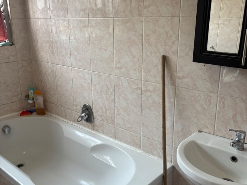 A functional bathroom featuring a built-in bathtub, pedestal basin, and wall-mounted mirror with neutral ceramic wall tiling.