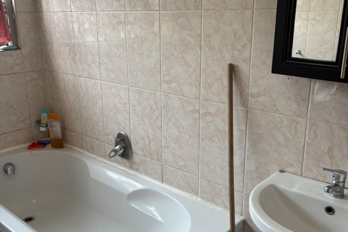 A functional bathroom featuring a built-in bathtub, pedestal basin, and wall-mounted mirror with neutral ceramic wall tiling.