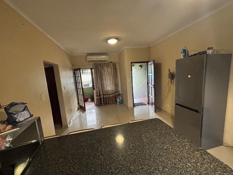 Open-plan living area featuring tiled flooring, a granite kitchen countertop, and a wall-mounted air conditioning unit with access to an outdoor patio.