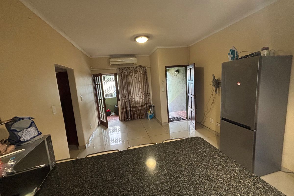 Open-plan living area featuring tiled flooring, a granite kitchen countertop, and a wall-mounted air conditioning unit with access to an outdoor patio.