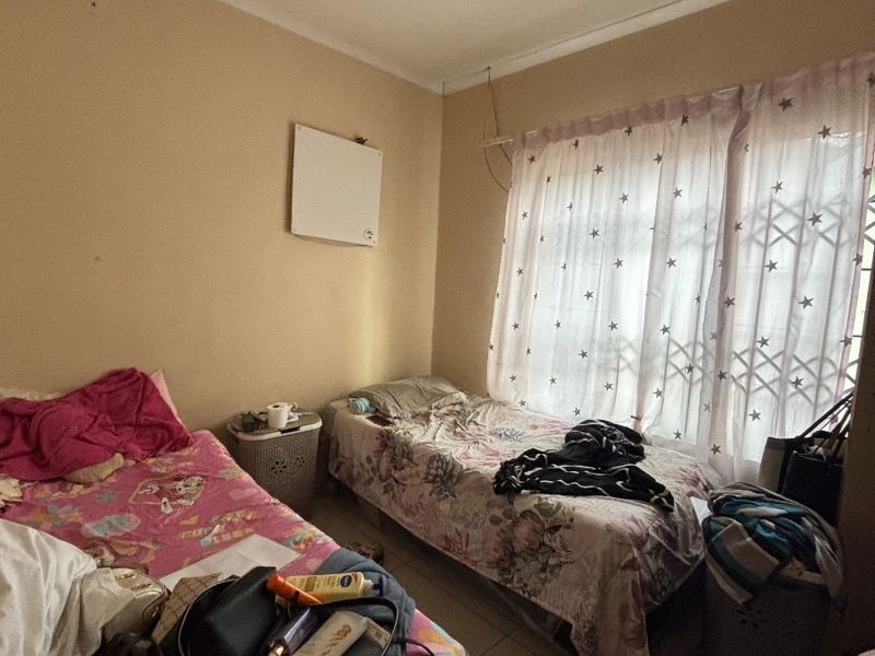 A bedroom featuring tiled flooring, a ceiling fan, and a wall-mounted heater, with a security gate installed over the window.
