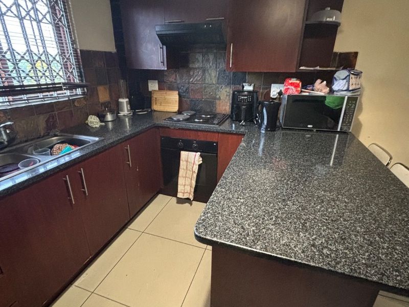 A functional kitchen featuring dark wood cabinetry, granite countertops, a built-in oven with hob, and a tiled backsplash.