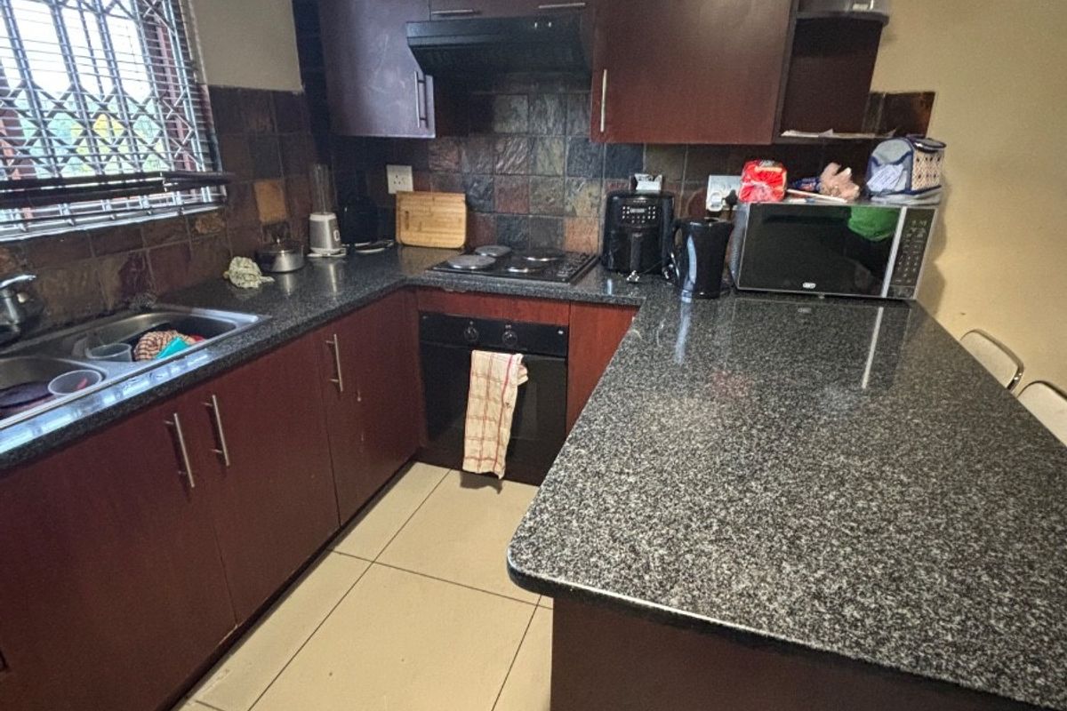 A functional kitchen featuring dark wood cabinetry, granite countertops, a built-in oven with hob, and a tiled backsplash.