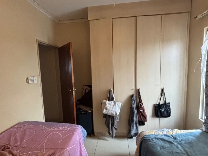 A bedroom featuring tiled flooring, a ceiling fan, and built-in cupboards with some visible wear on the cabinetry.