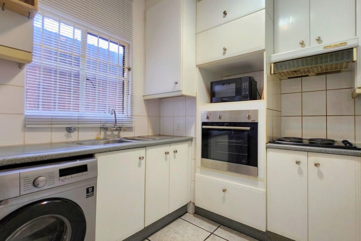 A functional kitchen featuring white cabinetry, built-in oven, electric hob, extractor fan, tiled backsplash, and a stainless steel sink with a window view.