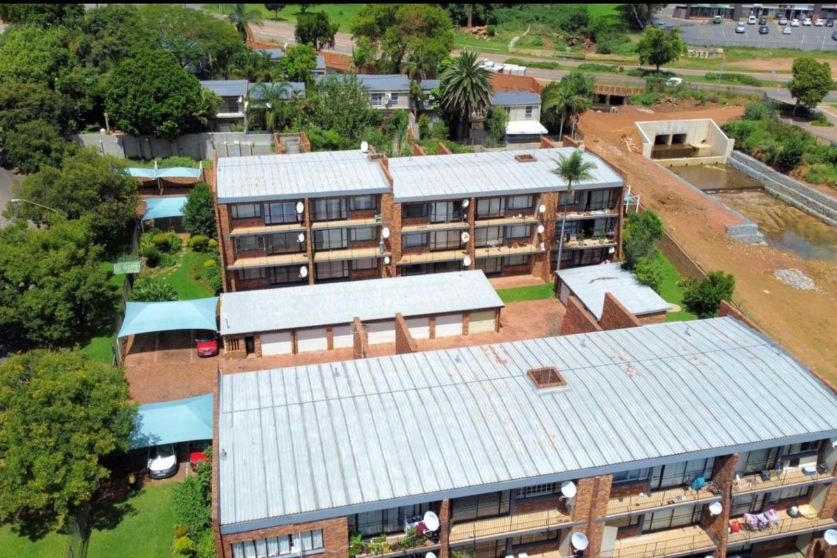 Aerial view of a multi-story apartment complex featuring brick facades, metal roofing, private balconies, and dedicated carport parking areas within a landscaped setting.