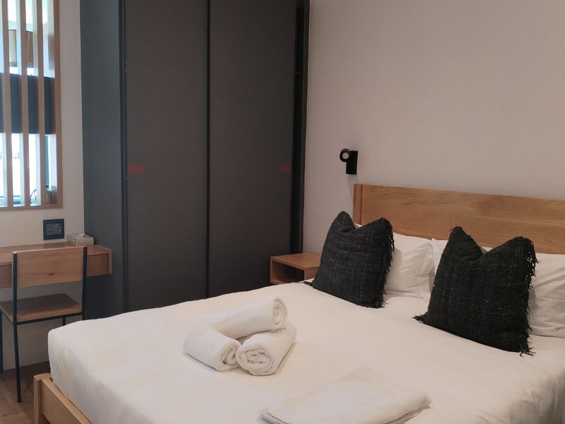 A modern bedroom featuring a timber headboard, built-in wardrobe, and integrated desk space with contemporary finishes and neutral tones.