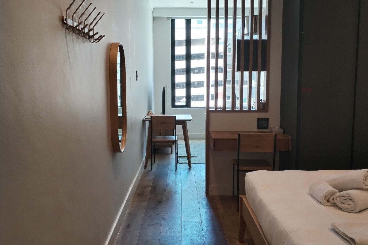 A modern bedroom featuring timber flooring, a built-in wardrobe, a functional desk area, and a stylish timber slat room divider.