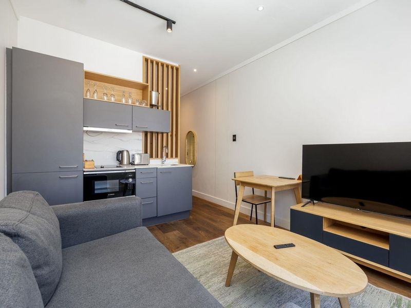 Modern open-plan living area featuring a compact kitchenette with sleek grey cabinetry, timber accents, and high-quality finishes throughout.