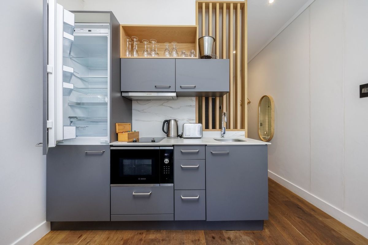 Modern compact kitchen featuring grey cabinetry, integrated appliances, stone countertops, and a decorative timber slat divider, set against hardwood flooring.