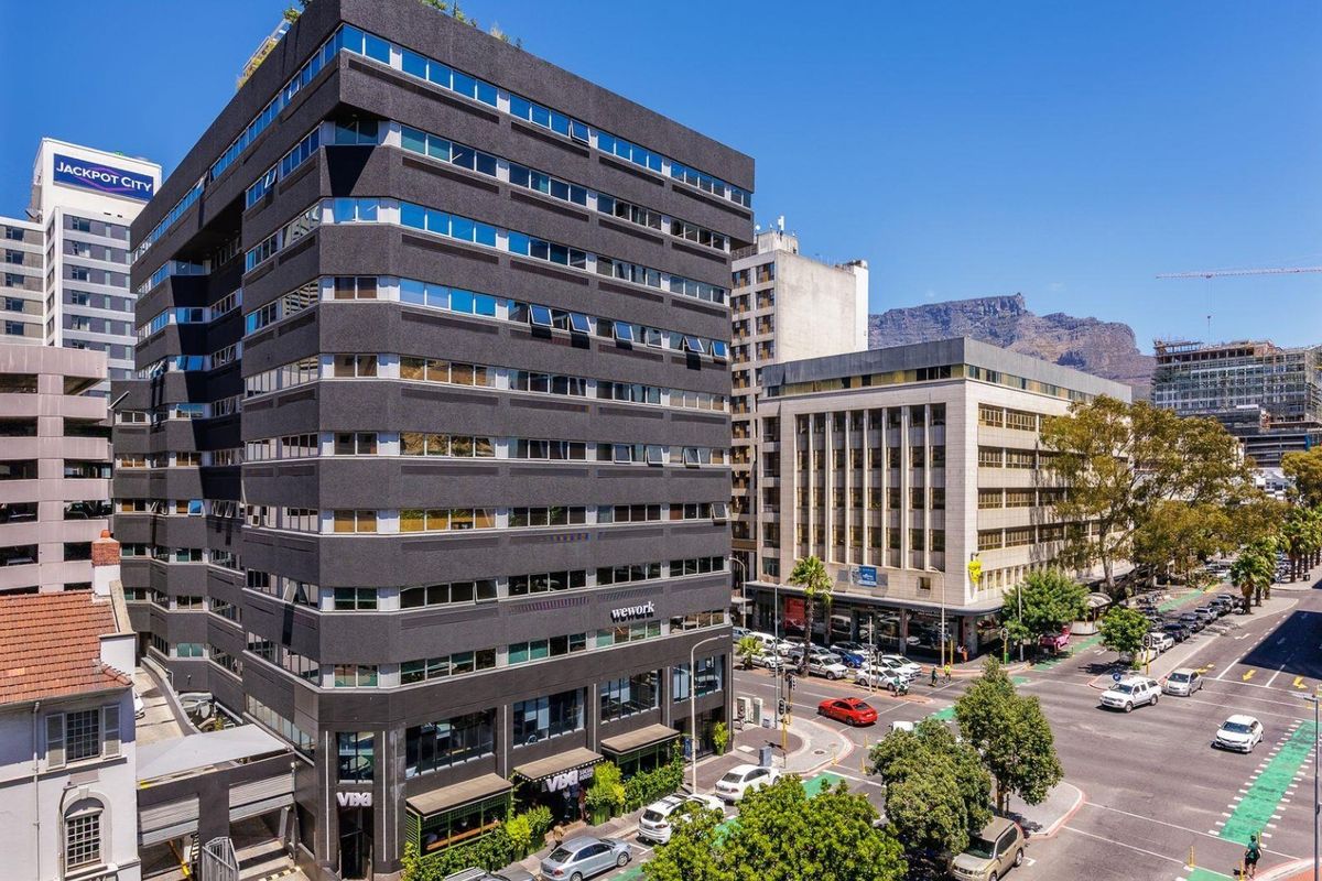 Aerial view of a modern multi-story commercial building in an urban setting with street-level retail and mountain views in the background.