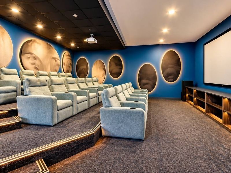 A professionally designed home cinema room featuring tiered seating, a large projection screen, integrated media cabinetry, and ambient recessed lighting.