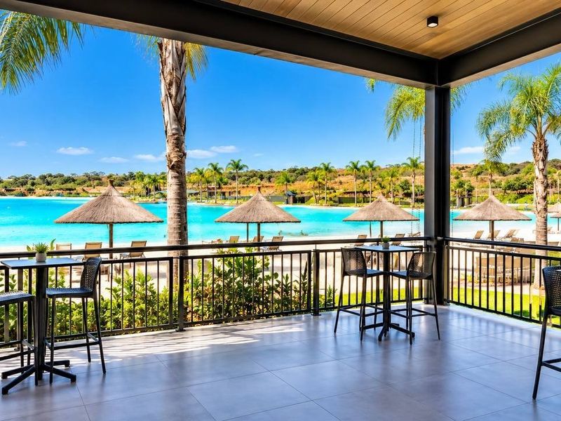 A spacious covered patio featuring tiled flooring and metal railings, offering direct views of a resort-style lagoon and landscaped surroundings.