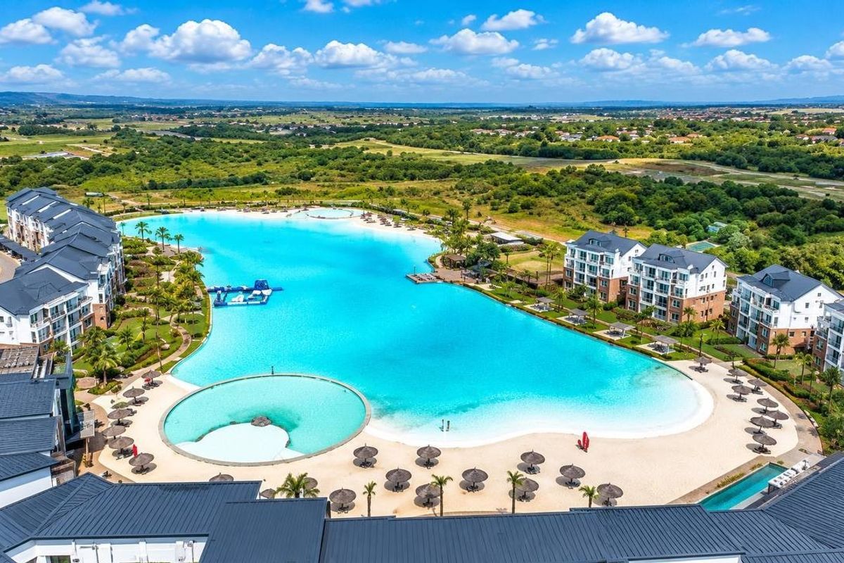 Aerial view of a modern apartment complex featuring a large central swimming lagoon, sandy beach area, and well-maintained landscaped grounds.