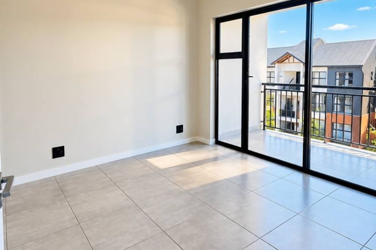 A bright, empty living area featuring modern neutral floor tiles, a single pendant light, and large sliding glass doors leading to a private balcony.