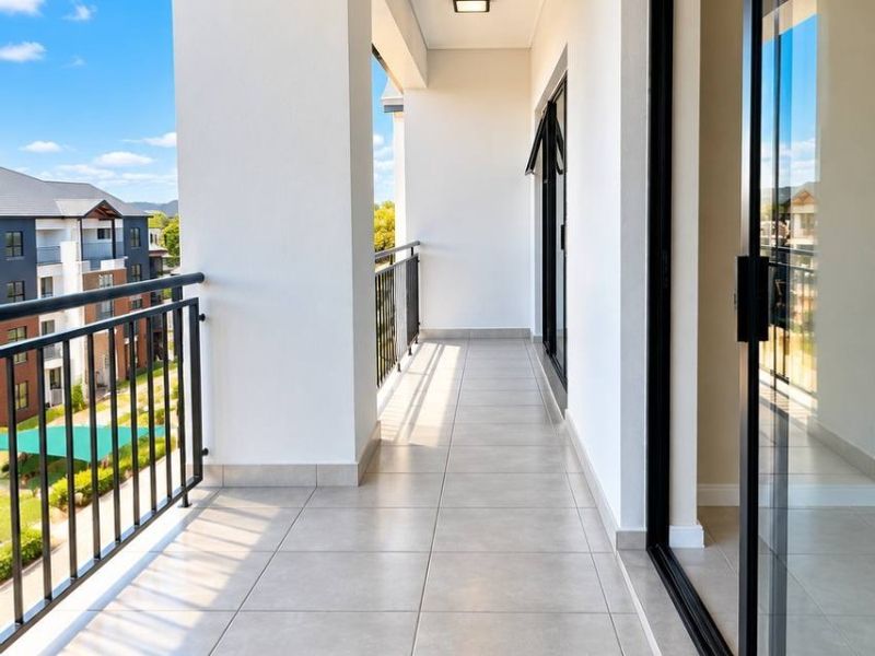 A clean, modern covered balcony featuring tiled flooring, a metal balustrade, and large sliding glass doors providing access to the interior.