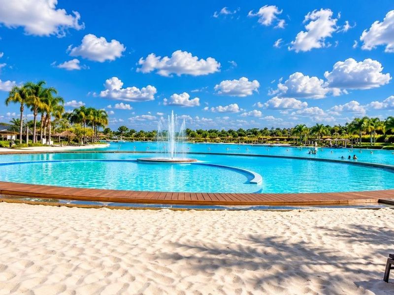 A large, well-maintained swimming pool area featuring a central water fountain, wooden decking, and a sandy beach-style perimeter.