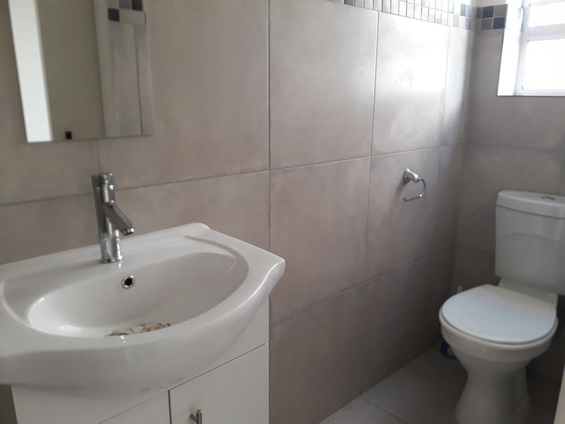 A clean, functional bathroom featuring a modern vanity with a basin, a wall-mounted mirror, and a standard toilet with neutral wall tiling.