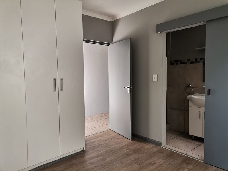 A clean, empty bedroom featuring modern laminate flooring, a built-in wardrobe, and direct access to an en-suite bathroom via a sliding door.