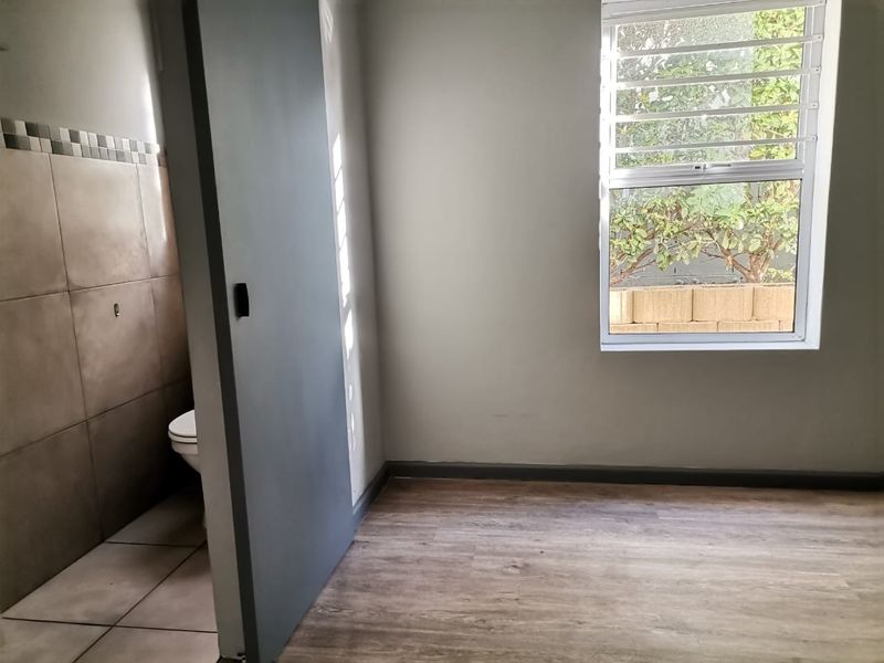 A compact, empty bathroom featuring tiled flooring, wall tiling, and a window with security bars, offering a clean and functional space.