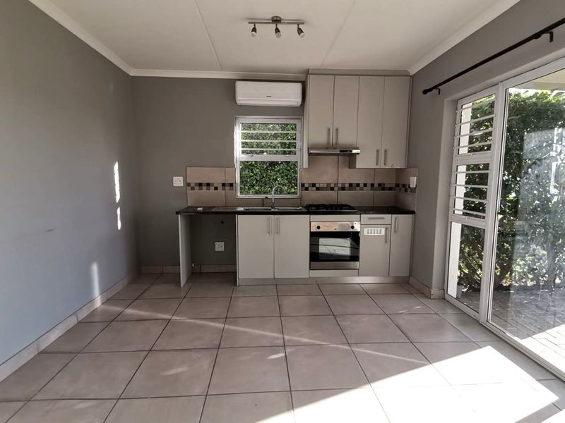 A clean, functional kitchen featuring built-in cabinetry, a gas hob, oven, extractor fan, and tiled flooring, with direct access to an outdoor area.