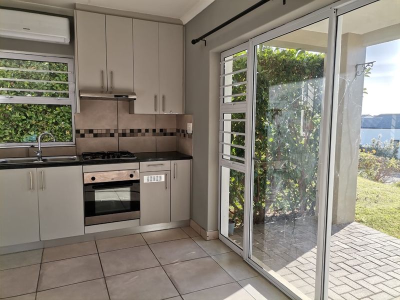 A clean, functional kitchen featuring built-in cabinetry, a gas hob, oven, and direct access to an outdoor patio area through sliding glass doors.