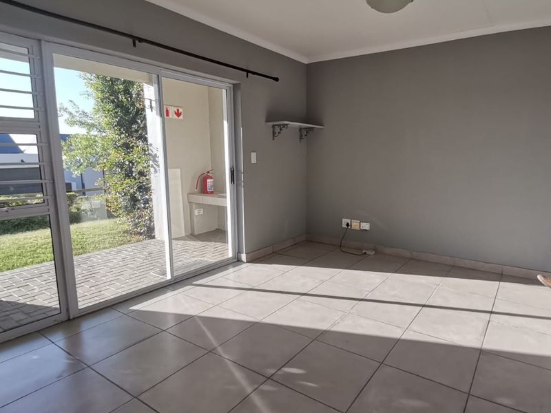 A bright, empty living room featuring neutral tiled flooring and a large sliding glass door providing access to an outdoor patio area.