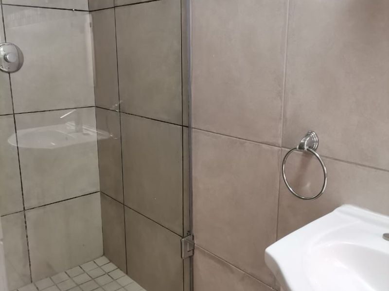 A functional bathroom featuring a glass-enclosed shower with tiled flooring and a vanity basin with a wall-mounted towel ring.
