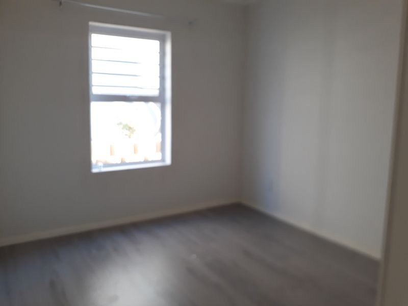 An empty bedroom featuring laminate flooring and a window with security bars, providing a blank canvas for personalization.