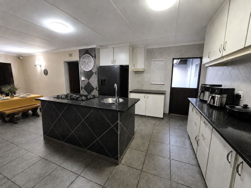 Open plan kitchen featuring a central island with gas hob and sink, granite countertops, and tiled flooring, seamlessly connecting to the dining area.