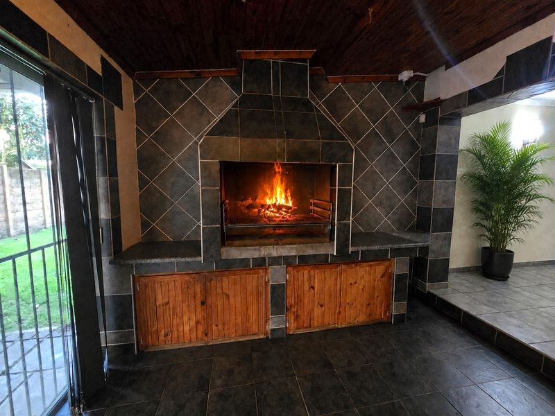 A covered patio area featuring a built-in braai with tiled surround, wooden cabinetry, and sliding glass doors leading to the garden.