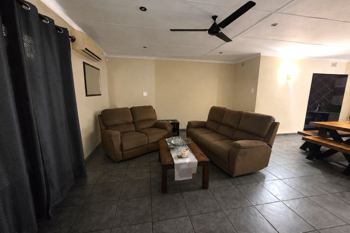 A spacious living area featuring tiled flooring, a ceiling fan, and a wall-mounted air conditioning unit, offering a functional and comfortable layout.