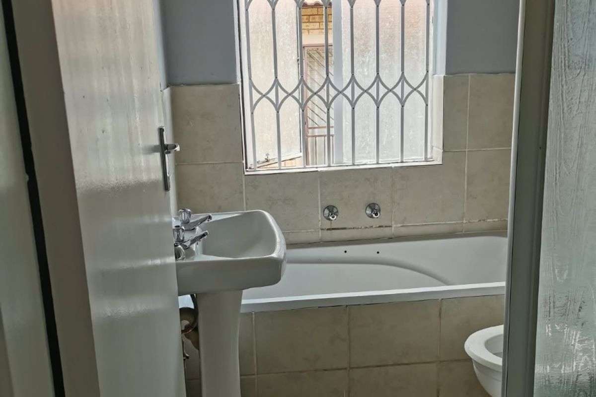 A functional bathroom featuring a pedestal basin, built-in bathtub, and shower enclosure, finished with tiled flooring and wall splashbacks.