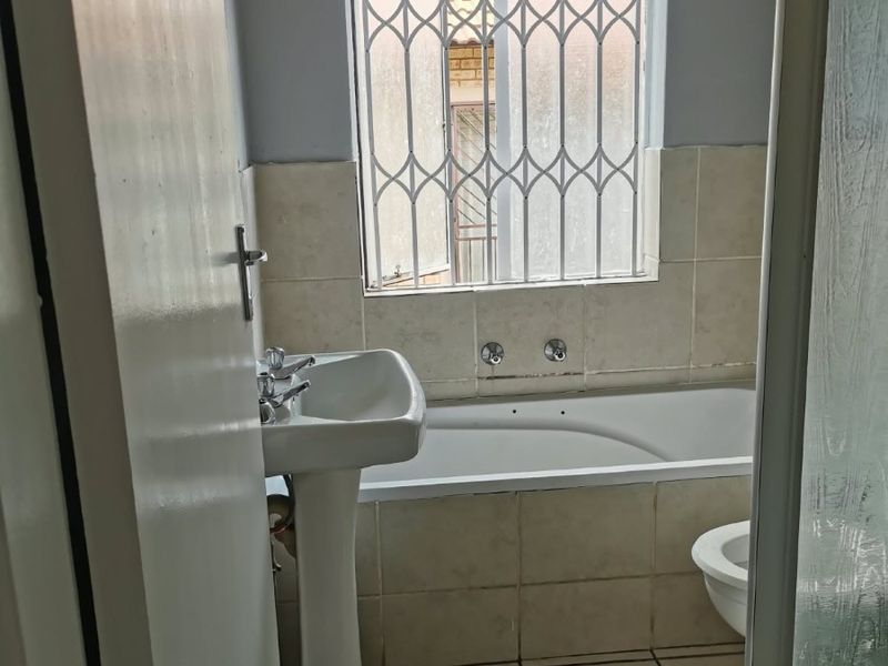 A functional bathroom featuring a pedestal basin, built-in bathtub, and shower enclosure, finished with tiled flooring and wall splashbacks.