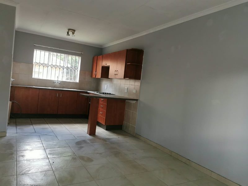 An empty kitchen featuring built-in wooden cabinetry, tiled flooring, a tiled backsplash, and a window with security bars.