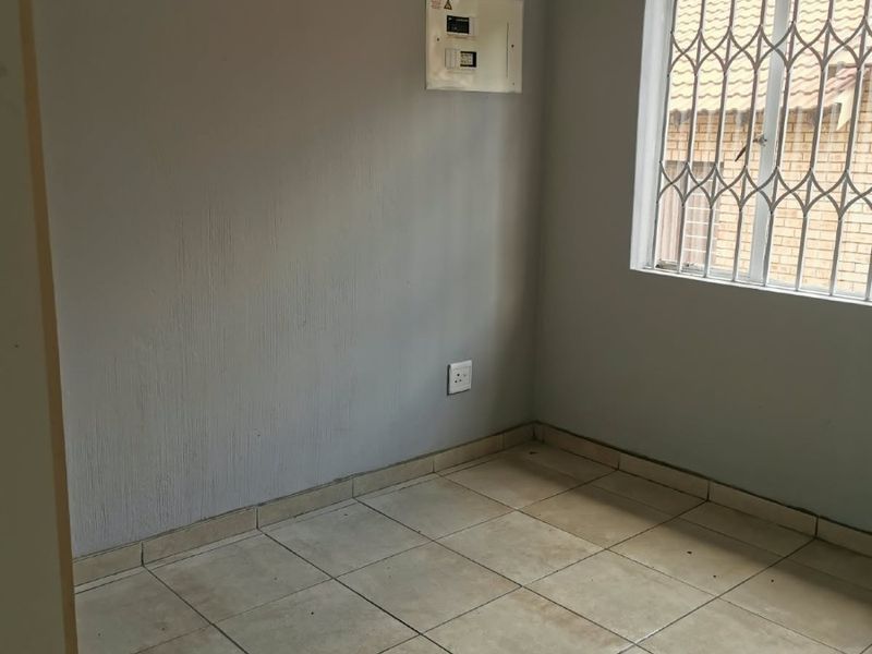 An empty bedroom featuring tiled flooring, a window with a security gate, and a wall-mounted electrical distribution board.
