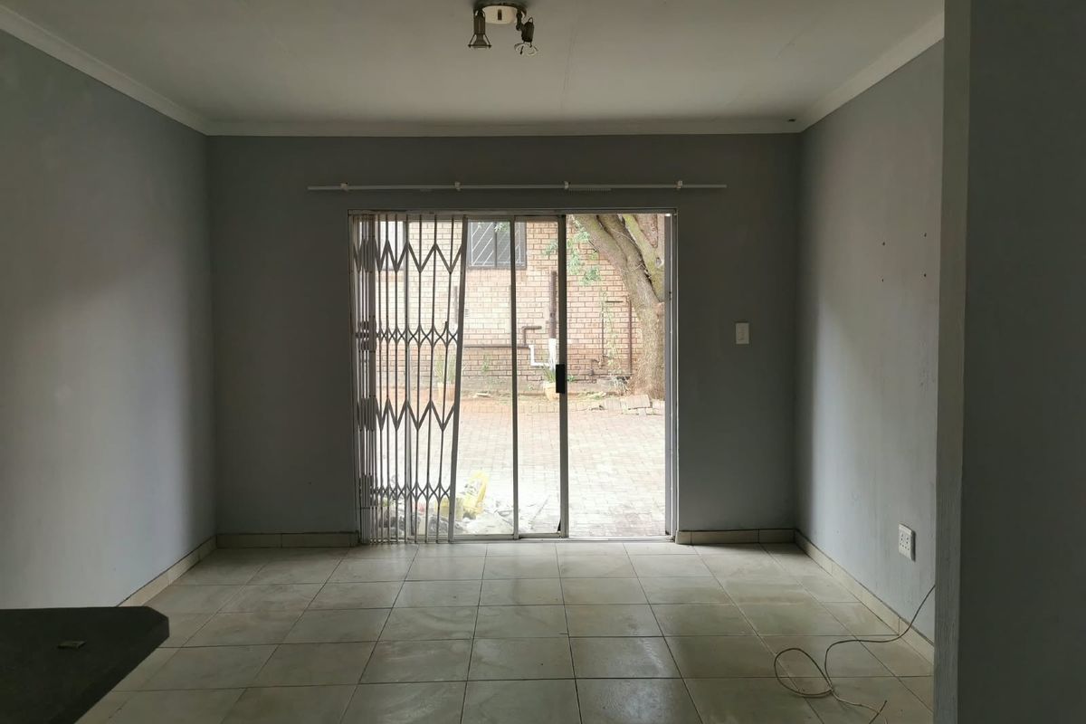 An empty, neutrally painted living area featuring tiled floors and a sliding glass door with a security gate leading to the rear patio.