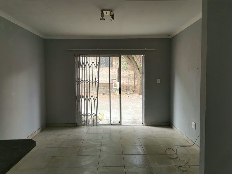 An empty, neutrally painted living area featuring tiled floors and a sliding glass door with a security gate leading to the rear patio.