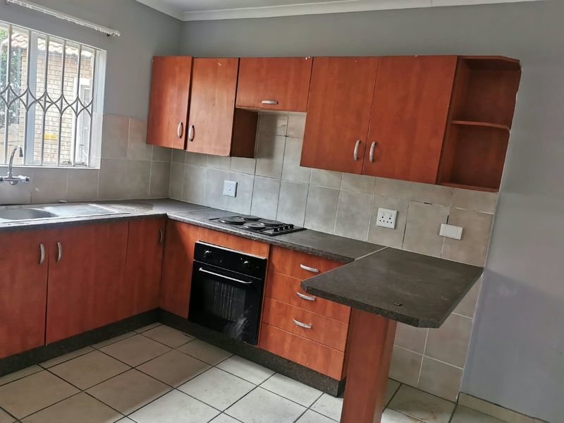 Functional kitchen featuring built-in wooden cabinetry, laminate countertops, integrated oven and hob, tiled backsplash, and a stainless steel sink with security window bars.