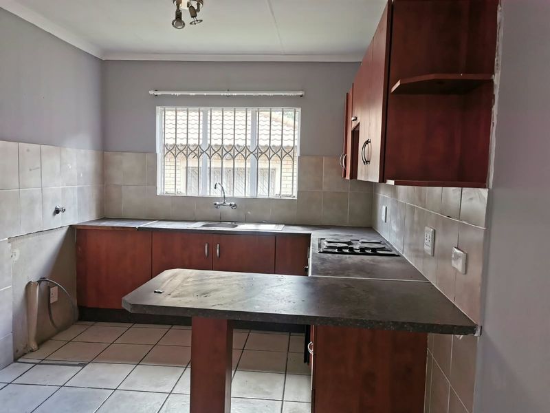 A functional kitchen featuring built-in cabinetry, a hob, and tiled finishes, currently vacant and ready for renovation or cosmetic updates.