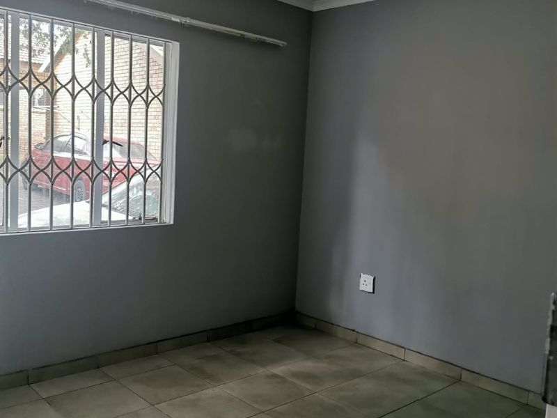 An empty bedroom featuring grey painted walls, tiled flooring, and security bars on the window, providing a blank canvas for potential interior design.