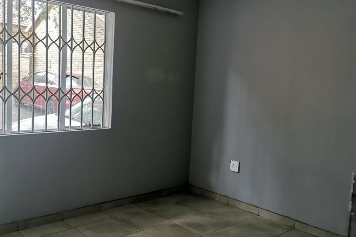 An empty bedroom featuring grey painted walls, tiled flooring, and security bars on the window, providing a blank canvas for potential interior design.